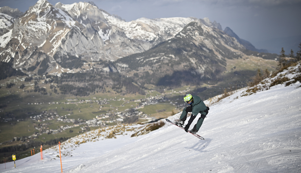 Ein Snowboarder in der Abfahrt vom Chäserrugg, mit Blick auf den Schafberg, im schneearmen Winter 2023.